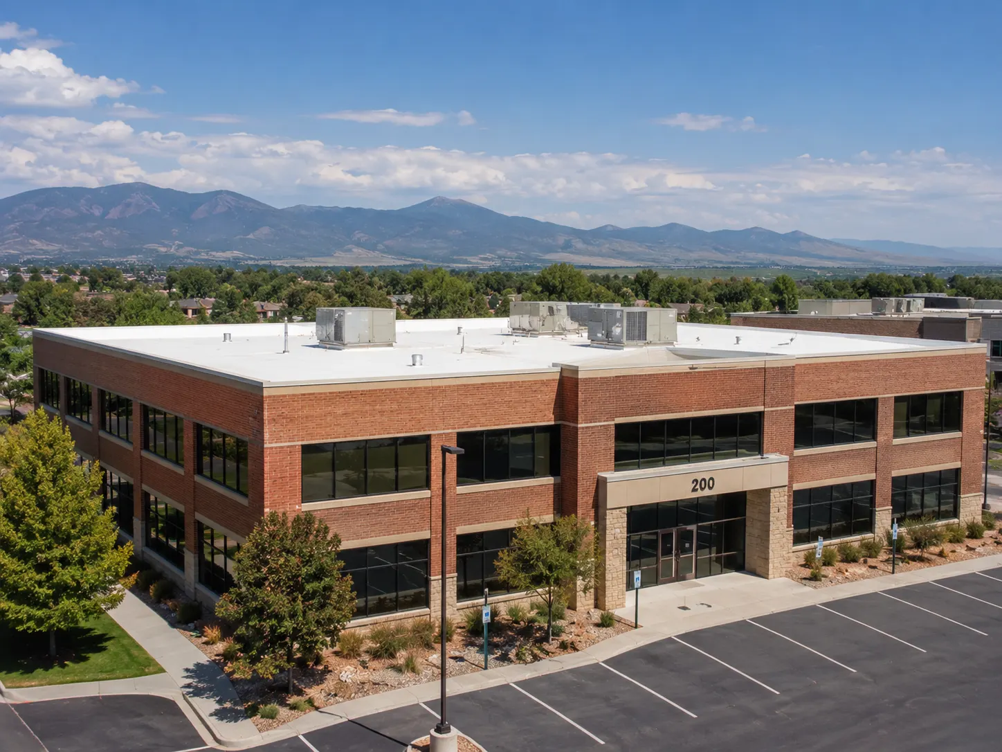 Two-story brick commercial building with a white TPO flat roof and Colorado foothills behind it in Parker